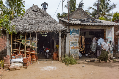Une hutte de palmes et un petit atelier s'appuient contre une maison au toit de tuiles.