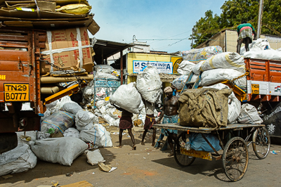 Hommes, camions et tricycles circulent entre d'impressionnantes montagnes de sacs de récupération.