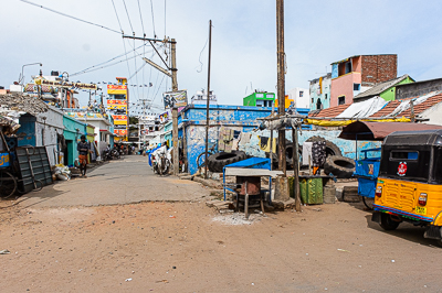 Un rickshaw traverse une petite rue commerçante où les boutiques se succèdent sans interruption.