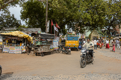 Motos, camion et échoppes se rencontrent à un carrefour ombragé.
