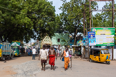 Une procession apparaît au bout de la rue, précédée par des hommes en dhoti coloré.