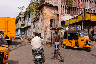 Un rickshaw s'engage dans une rue étroite bordée de vieilles maisons et de boutiques.
