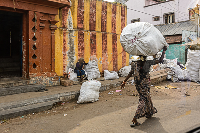Une femme transporte sur la tête un ballot démesuré devant un mur rayé de temple.
