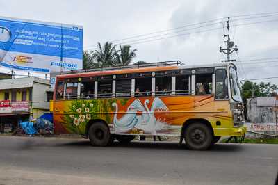 Un bus décoré de cygnes passe devant une publicité rédigée en malayalam.