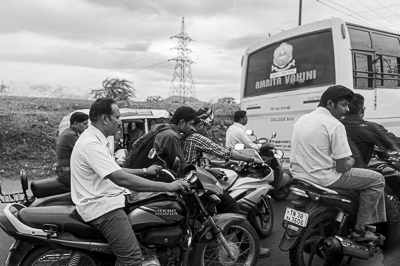 Des motocyclistes se pressent entre un rickshaw et un bus universitaire.