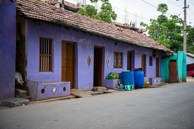 Une longue maison violette aux portes alignées, avec ses bidons d'eau posés sur le seuil.