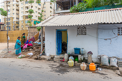 Des récipients d'eau bordent une petite maison bleue, dominée au loin par un immeuble récent.