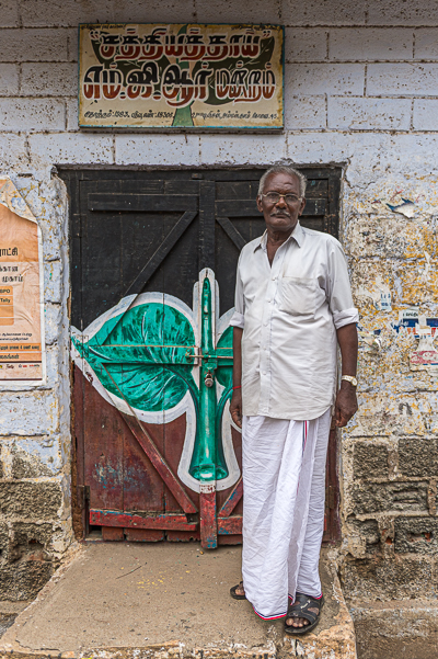 Un habitant pose devant le local du Sathiya Thai M.G.R. Mandram, dont la porte arbore l'emblème des deux feuilles de l'AIADMK.