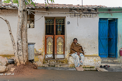 Une femme sourit, assise contre la façade blanche et bleue de sa maison.