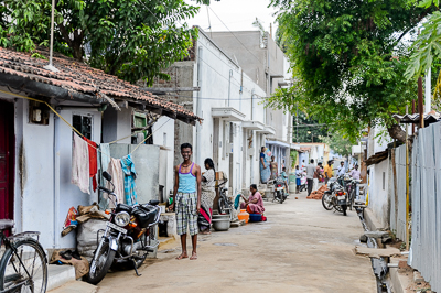 La ruelle dans toute sa profondeur, entre moto, linge étendu et habitants occupés devant leurs maisons.