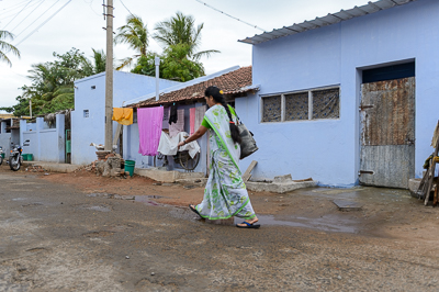 Une femme en sari traverse devant une maison bleue où le linge sèche en façade.