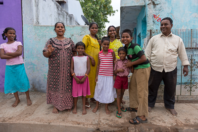 Une famille nombreuse, adultes et enfants réunis, pose devant une maison turquoise et violette.