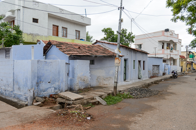Une rangée de petites maisons bleues borde une rue calme, avec ses caniveaux à ciel ouvert.