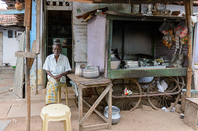 Un homme âgé est assis auprès d'une charrette équipée de casseroles et de récipients métalliques.