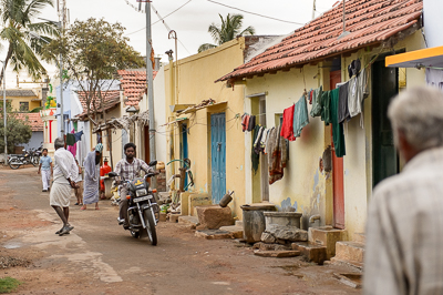 Une moto traverse une ruelle bordée de maisons jaunes aux portes bleues et de linge mis à sécher.