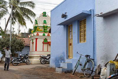 Le petit temple apparaît entre les cocotiers et une maison bleue, avec motos et bicyclette à ses pieds.