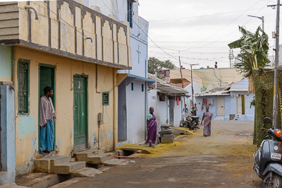 Dans la ruelle, les habitants restent sur les seuils tandis qu'une arche de palmes se dresse au bord de la rue.