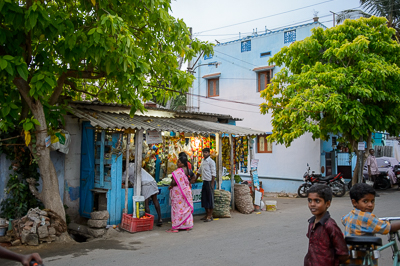 Sous les arbres, une épicerie de quartier attire les clients tandis que deux garçons regardent l'objectif.