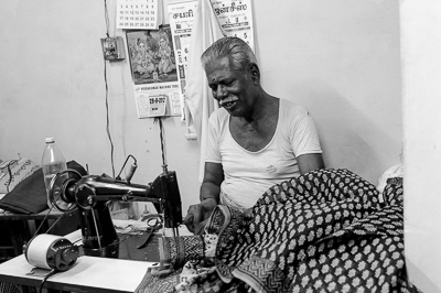 Portrait en noir et blanc d'un tailleur souriant derrière sa machine à coudre.
