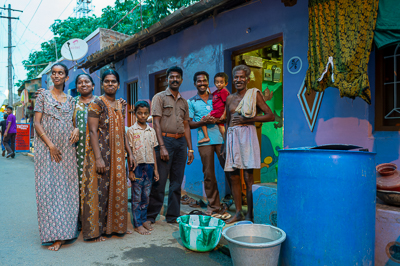 Une famille pose devant sa maison violette, entre linge suspendu, bassines et grands bidons d'eau.