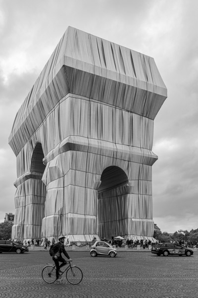 Un cycliste traverse la place au pied d’un Arc de Triomphe devenu presque irréel.