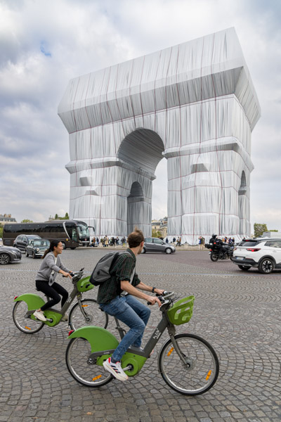 Deux Vélib passent devant le monument : le quotidien poursuit sa route autour de l’œuvre.