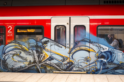 Le S-Bahn file vers la banlieue, ses passagers absorbés dans leurs pensées. Sur la carrosserie rouge, un graffiti déborde, mécanique et organique à la fois. La routine du trajet quotidien s’efface un instant, avalée par ce dessin sauvage qui transforme le train en fresque roulante.