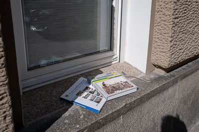 Deux manuels d’histoire reposent sur l’appui de fenêtre, comme abandonnés après révision. Mais à côté, une fourchette surgit, incongrue. Repas interrompu ? Pique-nique improvisé ? Ou simple hasard des trottoirs ? Stuttgart ajoute une note absurde à la banalité du décor