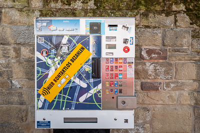 Fixée à la pierre comme un appendice moderne, la machine à cigarettes arbore ses couleurs criardes. Le slogan jaune claque : paiement sans contact, progrès plaqué sur une façade de vieille ville. Stuttgart juxtapose ainsi la rugosité des siècles et la consommation instantanée.