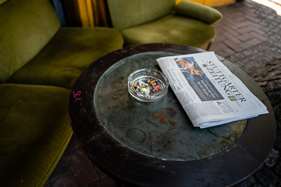Deux fauteuils verts attendent un retour, mais la scène dit tout : le cendrier déborde de mégots, le journal du jour traîne, plié sur la table ronde tachée d’empreintes. Le café s’est vidé, il ne reste que ce décor de fin de conversation, nature morte urbaine où Stuttgart fige l’instant après l’instant.