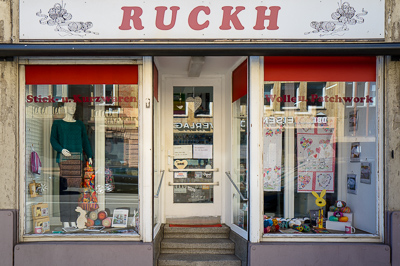 Tricot, patchwork, pelotes colorées et mannequin figé dans un pull vert : la vitrine raconte une autre époque, celle des merceries de quartier où l’on entrait pour demander un bouton ou une aiguille. Les reflets de la rue se mêlent aux tissus et aux lapins décoratifs. À Stuttgart, ce magasin semble tenir bon, hors du temps, comme un petit musée de la vie quotidienne.