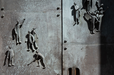 On dirait une foule miniature saisie dans le métal : un homme salue, un autre se penche, des groupes se forment, les bras s’élèvent. Ces personnages de bronze, incrustés dans la porte, semblent rejouer les gestes éternels de la rue : marcher, attendre, discuter, lever la tête. À Stuttgart, même les passants sculptés ont leur vie propre..