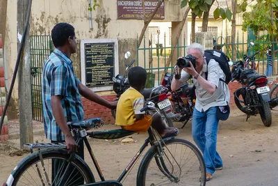 Appareil devant l’œil et jambes fléchies, je photographie un homme tenant un vélo sur lequel un enfant en jaune est assis.