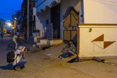 À la tombée du jour, je m’accroupis pour photographier un homme assis devant une grille, au coin d’une maison.
