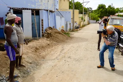 Jambes écartées et appareil devant l’œil, je photographie deux hommes portant des tissus noués sur la tête, devant une maison bleue.