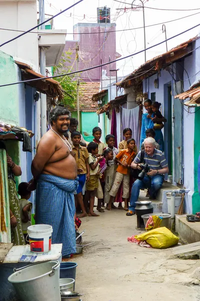 Assis sur une marche avec mon appareil, je suis entouré d’enfants dans une ruelle colorée ; un homme en tissu bleu noué à la taille sourit au premier plan.