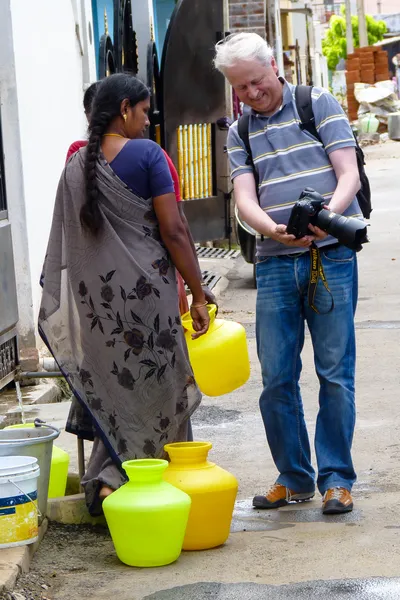 Je montre la photographie sur l’écran de mon appareil à une femme en sari gris tenant un récipient jaune, près de plusieurs bidons posés au sol.
