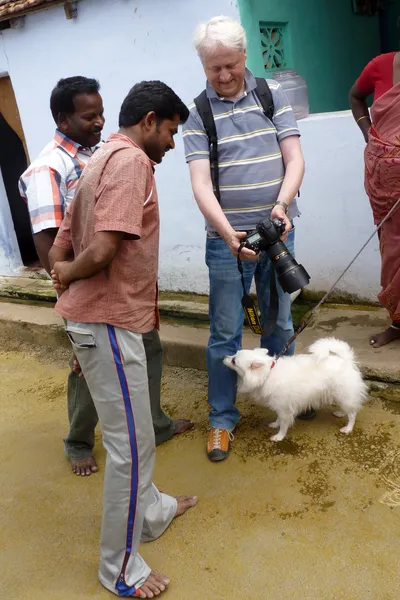 Je montre la photographie sur l’écran de mon appareil à deux hommes tandis qu’un petit chien blanc se tient à mes pieds ; une femme apparaît à droite.
