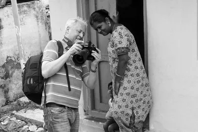En noir et blanc, je montre la photographie sur l’écran de mon appareil à une jeune femme appuyée dans l’encadrement d’une porte.