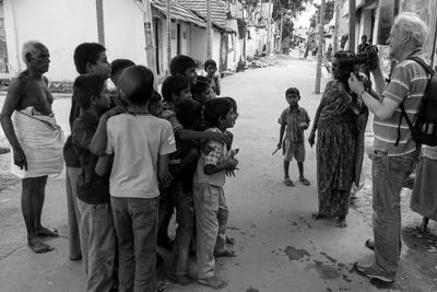En noir et blanc, je tiens mon appareil face à un groupe d’enfants réunis dans la rue, près d’une femme et d’un homme plus âgé.
