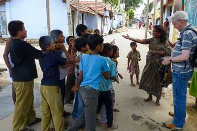 Appareil abaissé, je regarde une femme tendre le bras vers un groupe d’enfants rassemblés dans une rue bordée de maisons colorées.