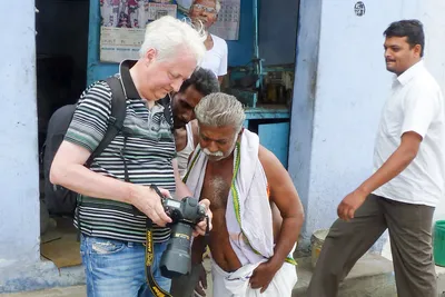 Je montre la photographie sur l’écran de mon appareil à deux hommes devant une boutique bleue, tandis qu’un passant en chemise blanche traverse la scène.