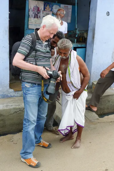 Devant une boutique bleue, deux hommes se penchent pour regarder la photographie sur l’écran de mon appareil ; celui du premier plan porte un tissu blanc noué à la taille.