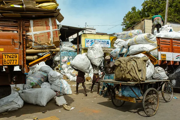Des camions chargés de sacs et de cartons, une charrette, des ballots posés au sol. Plusieurs hommes travaillent au milieu de cet encombrement.