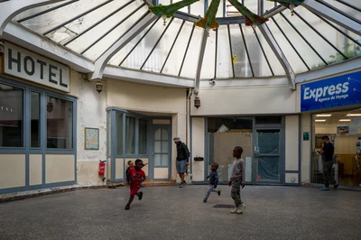 Un enfant vêtu de rouge court sous la verrière, tandis que d’autres enfants et des adultes occupent le passage devant la boutique Express.