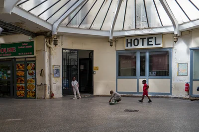 Trois enfants devant l’hôtel du passage du Prado : l’un près de la porte, un autre accroupi au centre et un troisième vêtu de rouge.