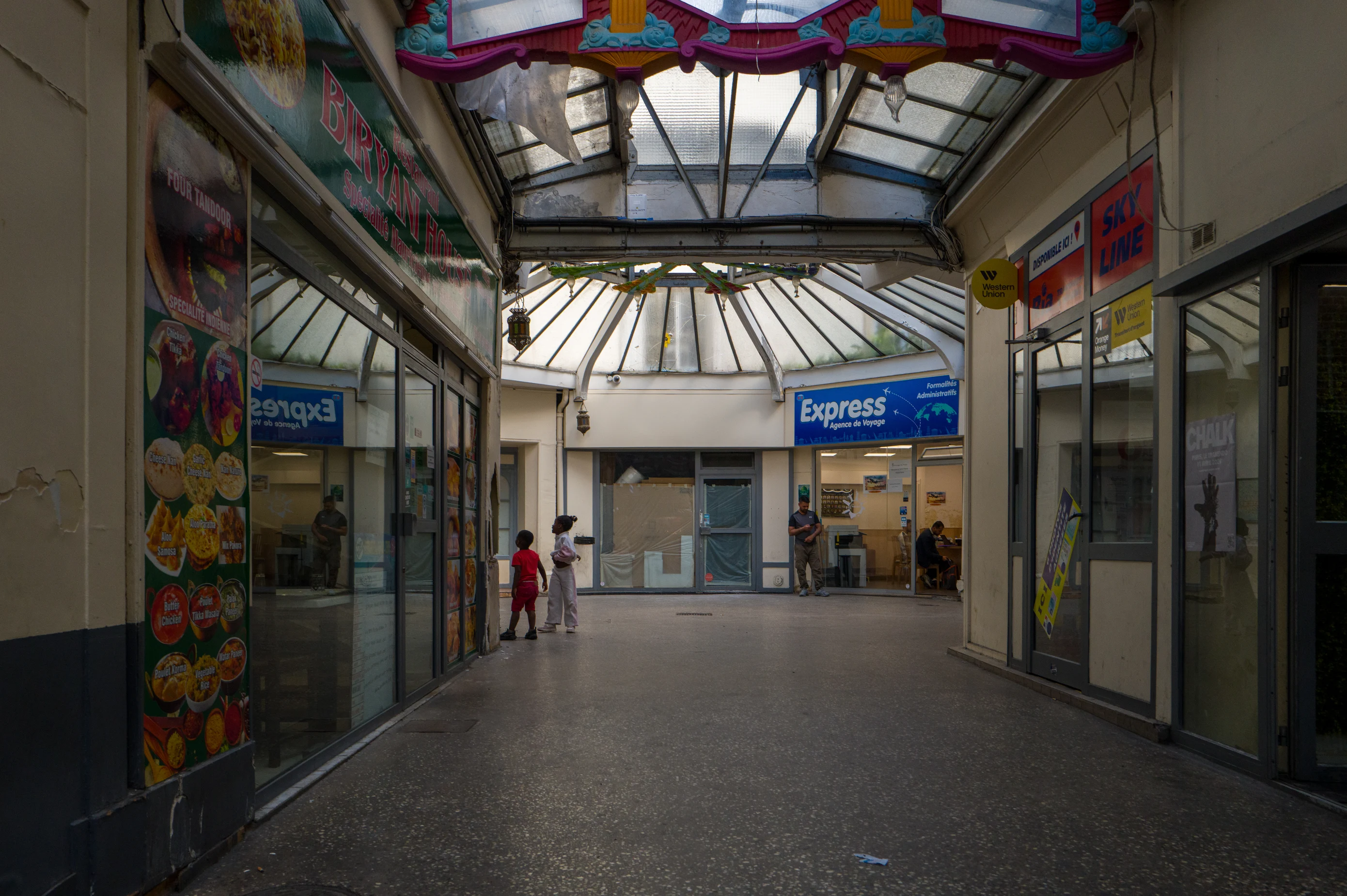 Vue en longueur du passage du Prado, bordé de vitrines, sous les verrières et leurs ornements colorés.